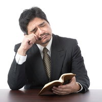 本を読みながら過労からくる疲れ目で頭を抱える中年男性の写真