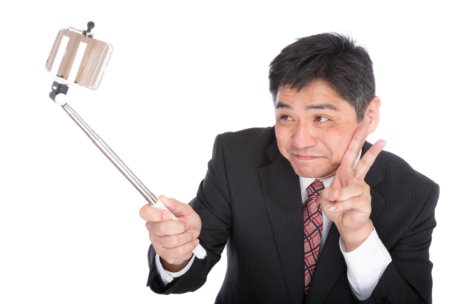セルフィースティックでスマートフォンを持ちピースサインをしながら自撮りする紺色スーツの中年男性［モデル：よたか］
