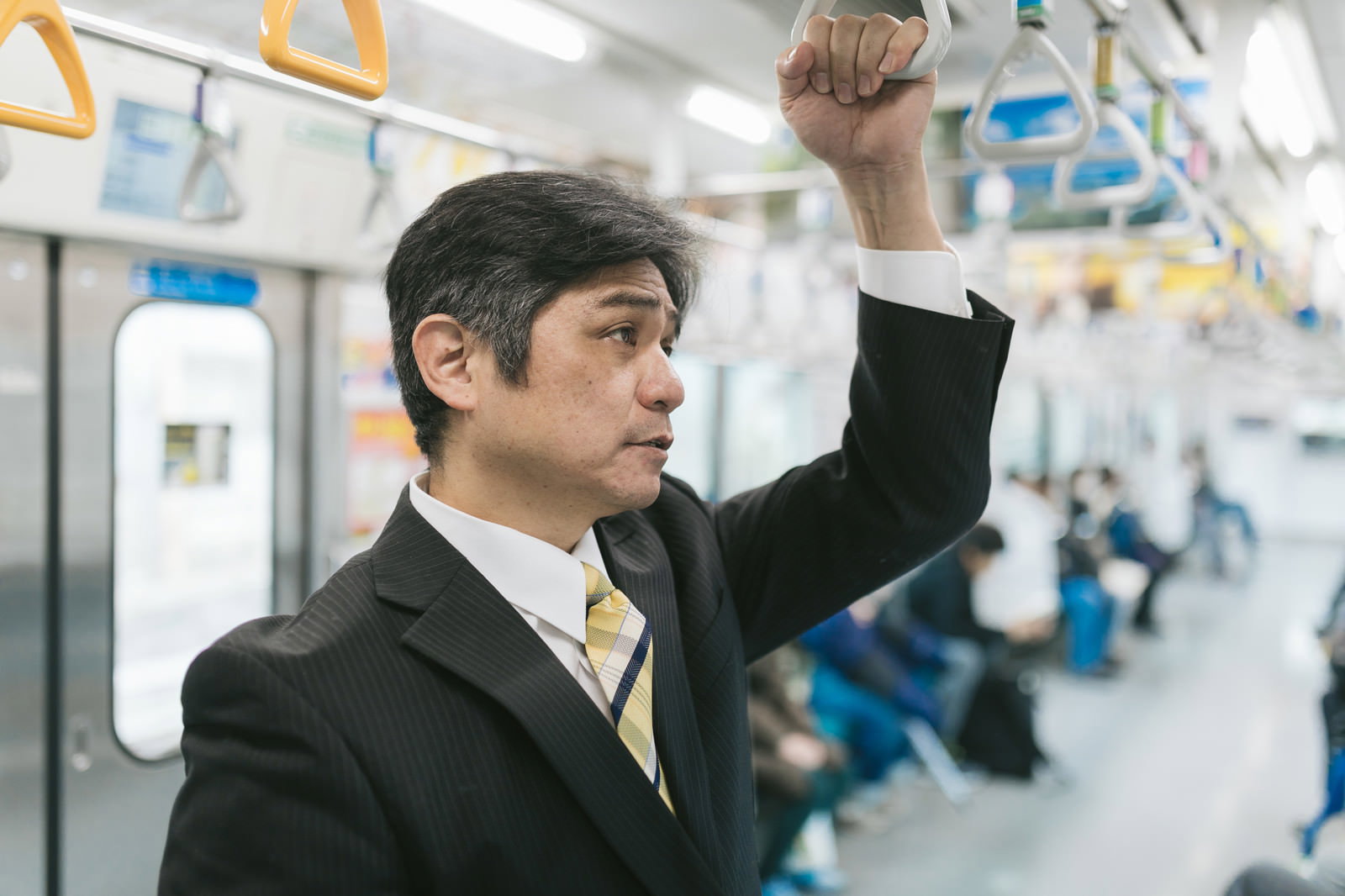 電車内で吊革につかまりながら立っているスーツ姿の男性［モデル：よたか］
