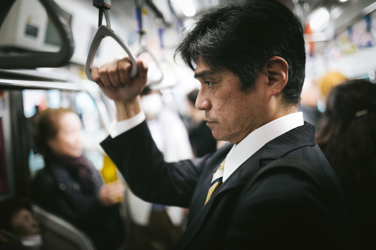 満員電車内で吊革につかまるスーツ姿の中年男性