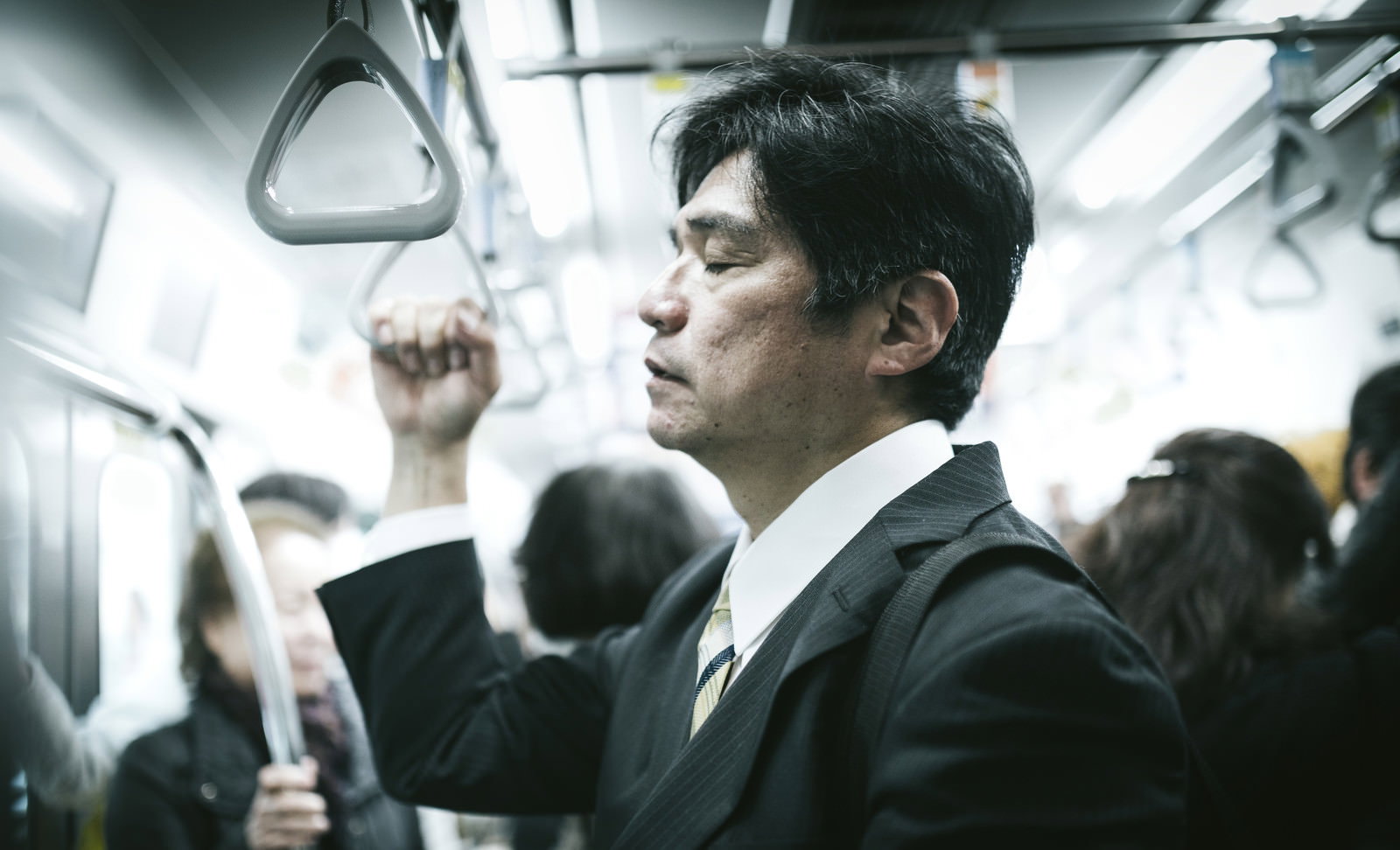 満員電車の中で吊革を握りながら立ったまま寝ている疲れたスーツ姿の中年男性