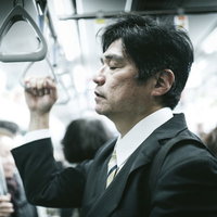 電車の中で吊革を握りながら立ったまま寝る中年男性の写真