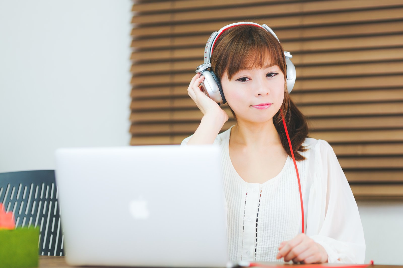 ヘッドフォンをつけてノートパソコンで作業する女性［モデル：暢子］