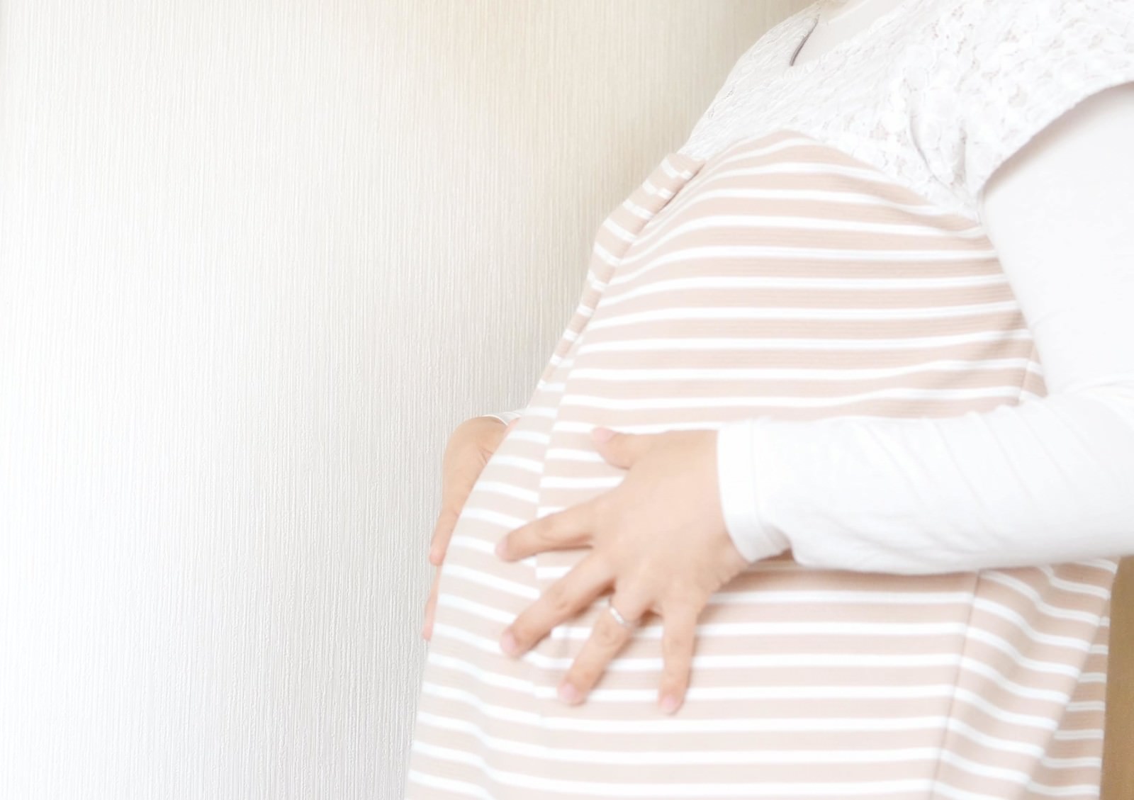 妊婦がピンクのボーダー柄マタニティトップスを着てお腹を触れている