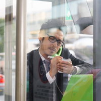 待ち合わせ前に相手の特徴をメモしながら電話ボックスで通話する会社員の写真