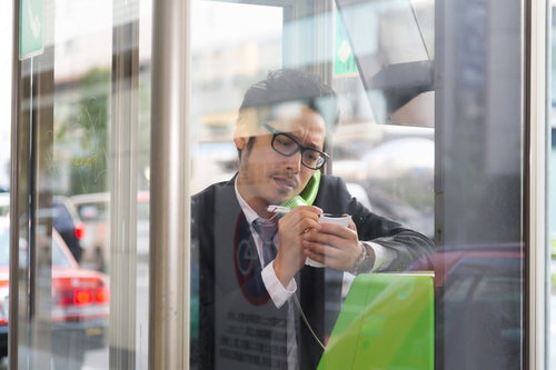 待ち合わせ前に相手の特徴をメモしながら電話ボックスで通話する会社員