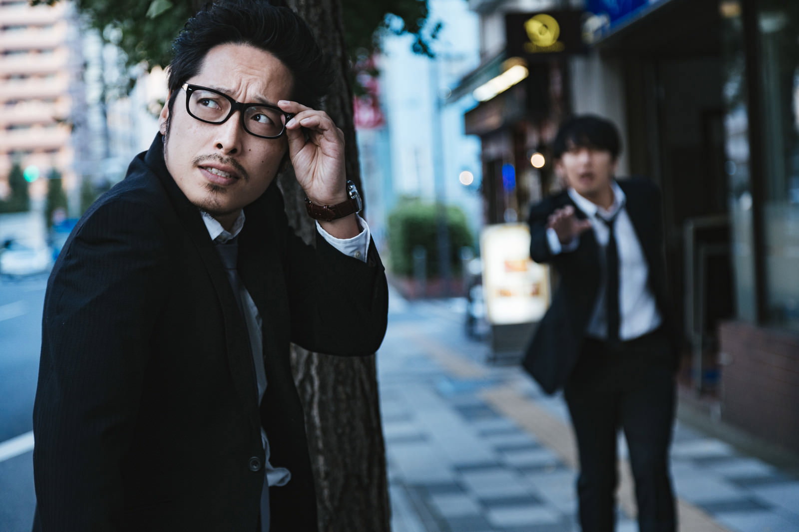 夜の街で携帯電話で通話するスーツ姿の眼鏡をかけた男性［モデル：大川竜弥 ゆうせい］