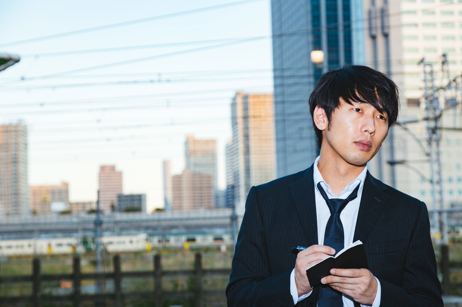 都市部でスマートフォンを見つめる黒いスーツ姿の男性［モデル：大川竜弥］