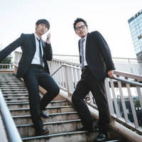 ノルマに追われる後輩とノルマを諦めた先輩、歩道橋で休憩する2人のビジネスマンの写真