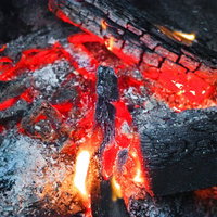 燃え尽きかけた薪と赤い炭火のクローズアップの写真