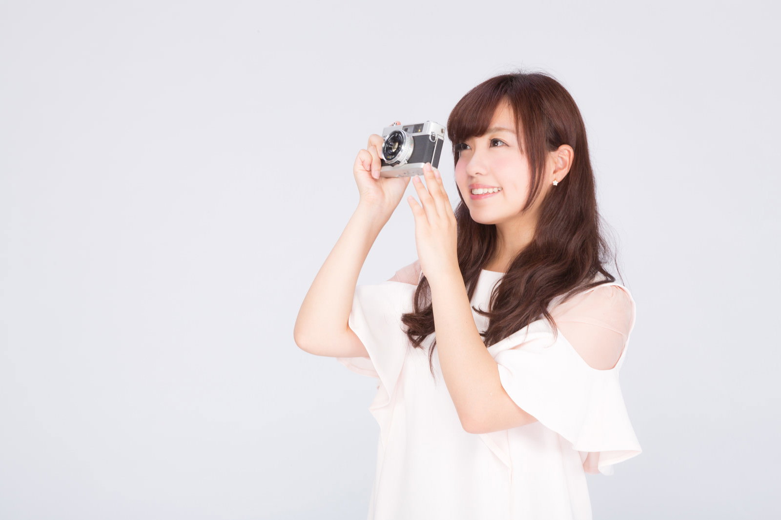 白いトップスを着た茶髪の女性がフィルムカメラを構えて撮影している様子［モデル：河村友歌］