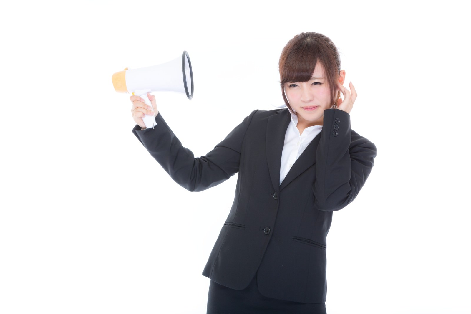 スピーカーを持ち上げながら片手で耳を塞いで嫌そうな表情の黒いスーツの女性社員［モデル：河村友歌］