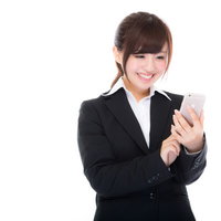 就業中にスマホで株式投資の利益確定をするスーツ姿の女性の写真