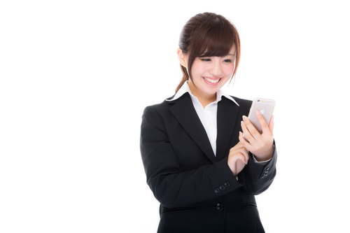 就業中にスマホで株式投資の利益確定をするスーツ姿の女性