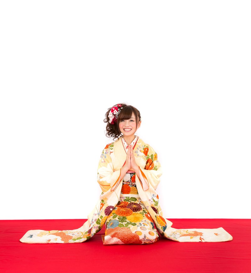 赤い舞台に座り笑顔で正面を向く、花柄振袖姿の女性［モデル：河村友歌］