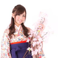 淡いピンクの桜の枝を持つ着物姿の笑顔の女性の写真