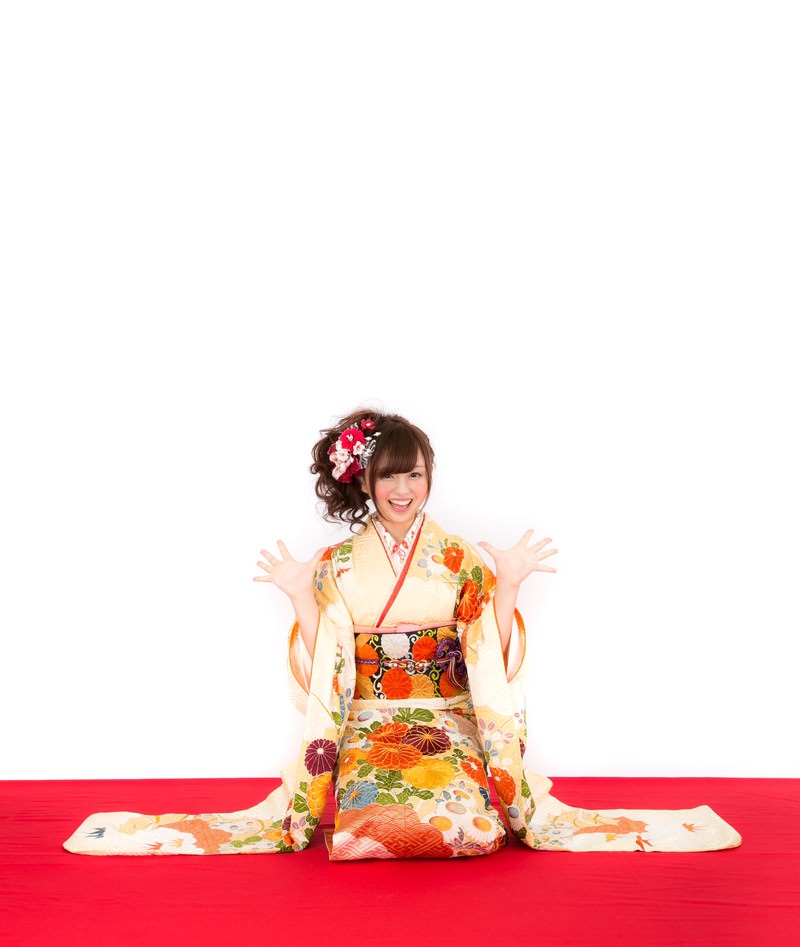 赤い布の上で両手を広げて笑顔で喜ぶ振袖姿の女性［モデル：河村友歌］