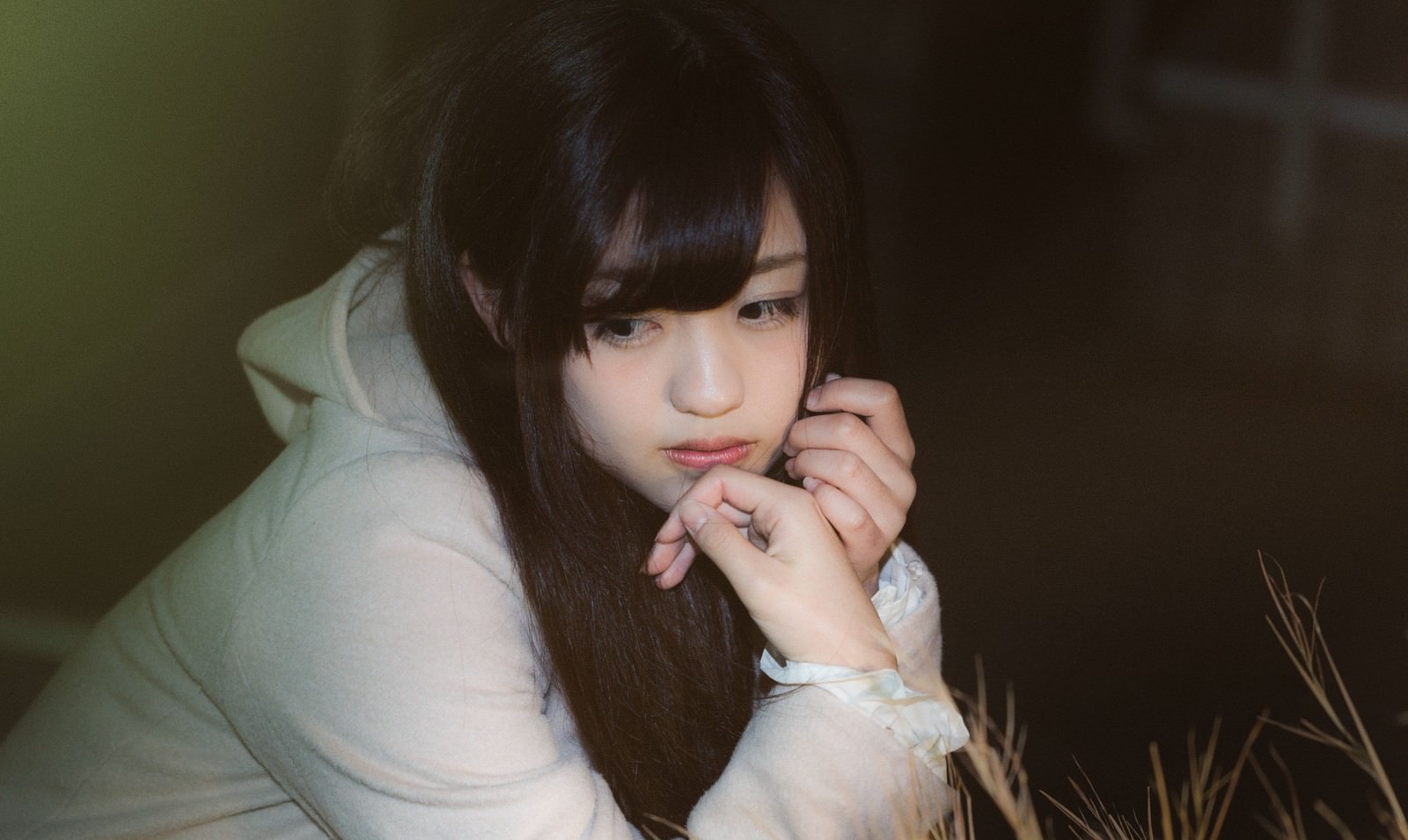 身体を丸めて考え込む黒髪の女性。悩ましい表情で両手を顔に寄せている［モデル：河村友歌］