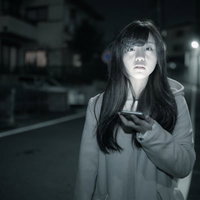 嫁が夜な夜な出かけて行きます。深夜の街でスマホを片手に歩きスマホする女性の写真