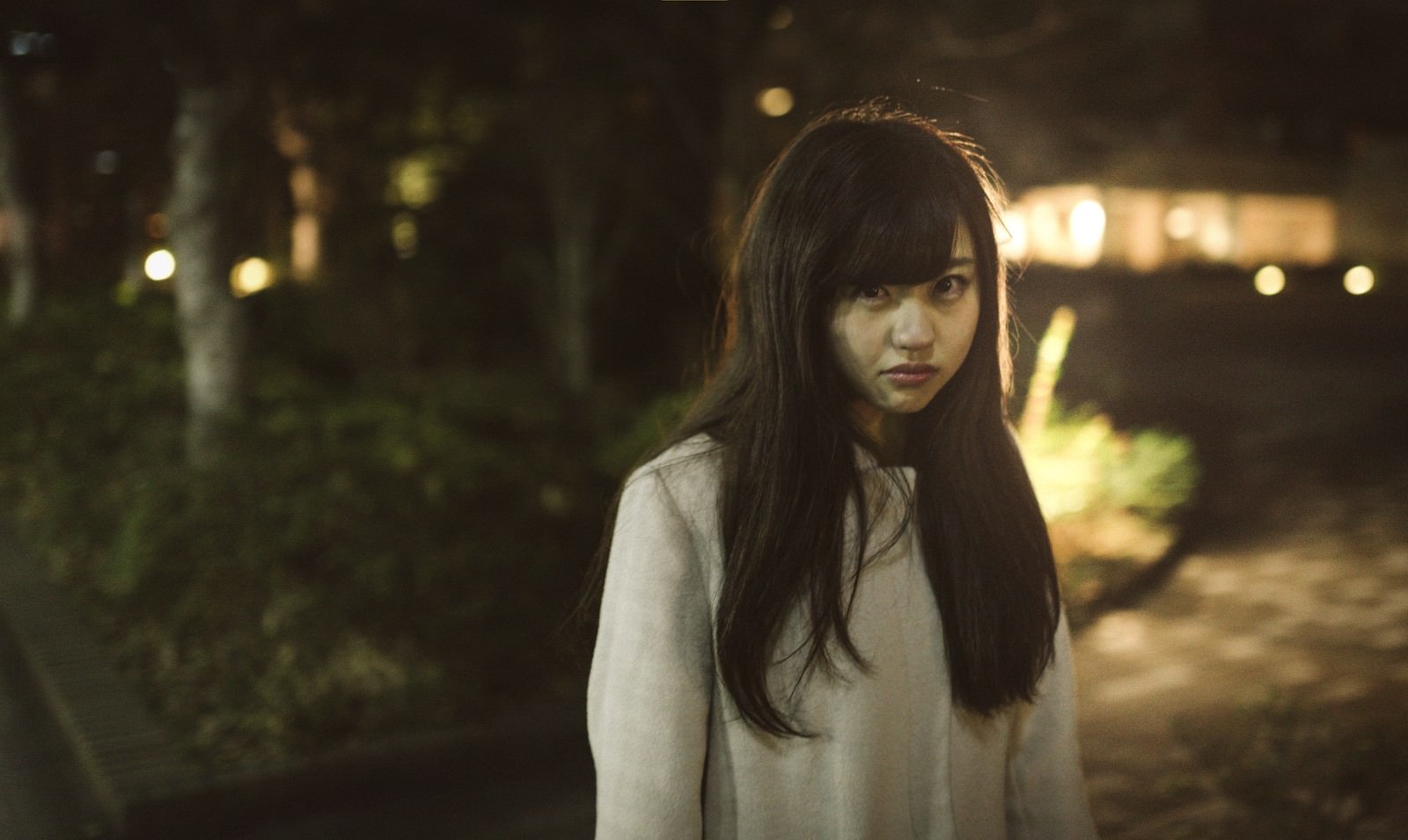 夜間の街路で怒りをあらわにする長髪女性が白いシャツを着て正面を見つめている［モデル：河村友歌］