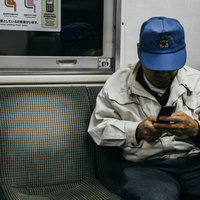 ローカル線で携帯を操作する作業着姿の年配者の写真