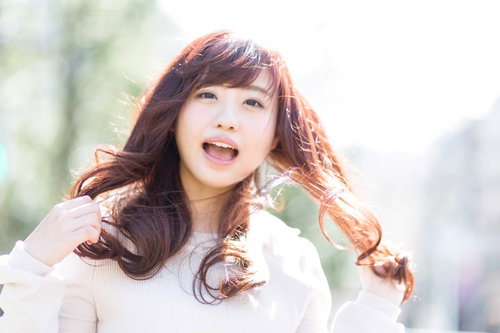 太陽光の中で髪をかき上げて笑うキラキラ女子