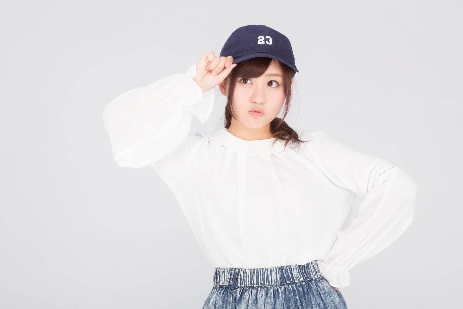紺キャップと白トップスの女性がつばに手を当てるポーズ［モデル：河村友歌］