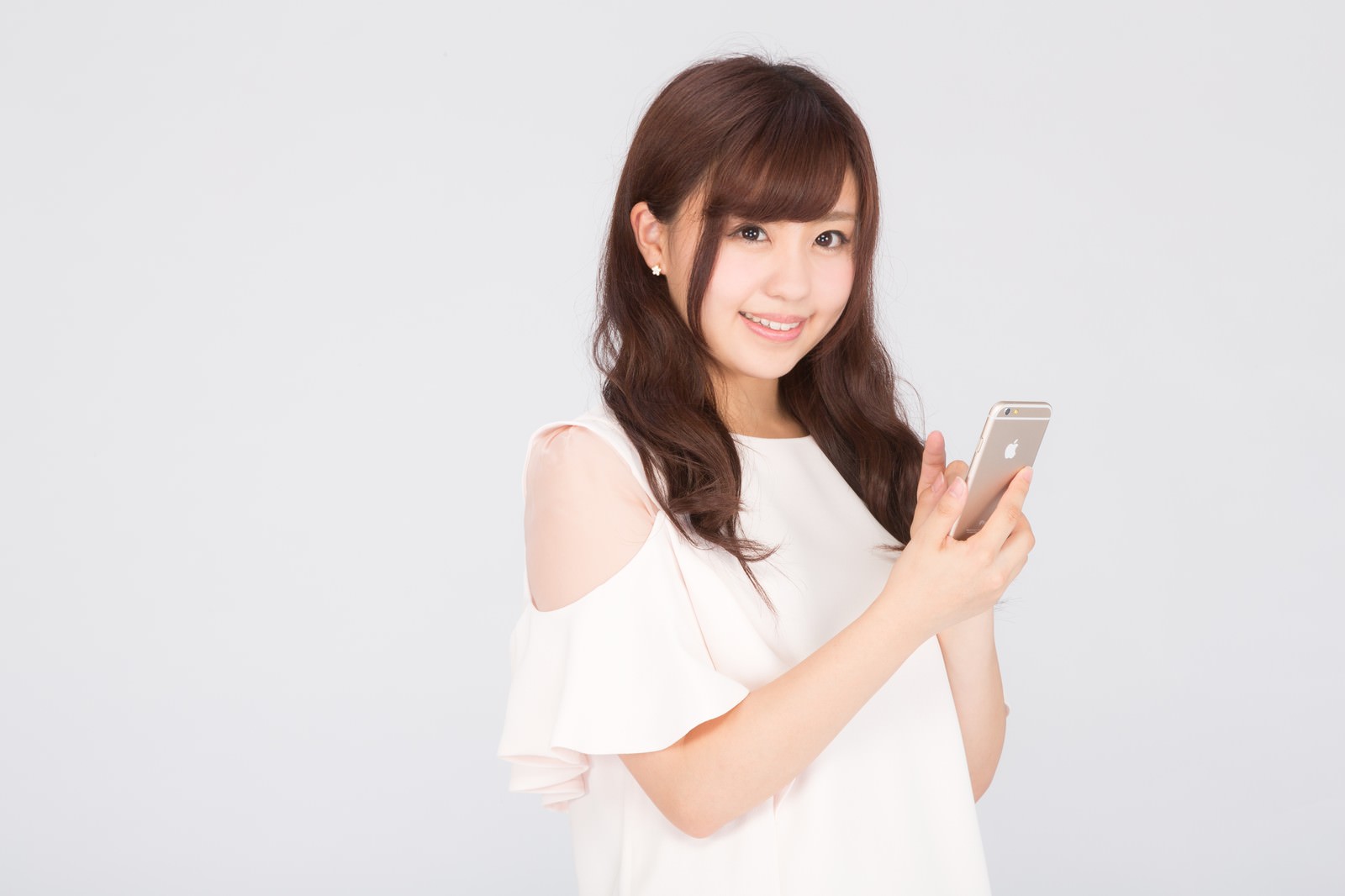 白いオフショルダートップを着た女性がスマートフォンの画面を見て笑っている［モデル：河村友歌］