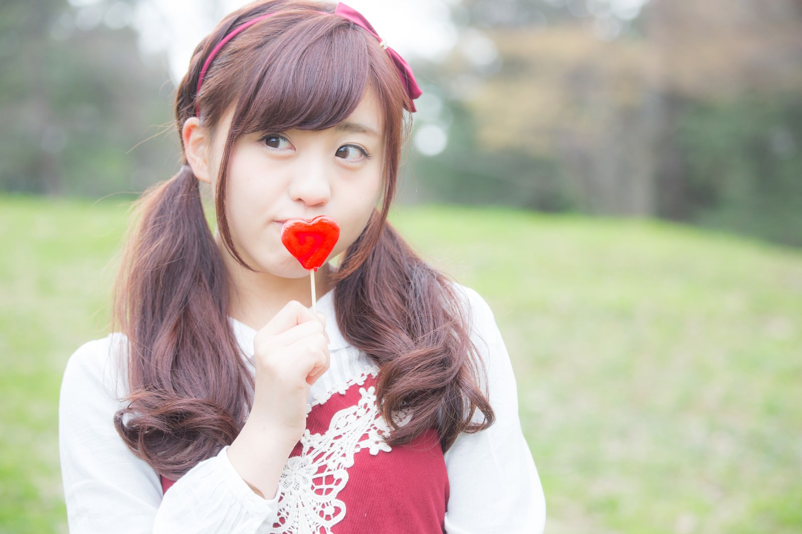 ハート型のキャンディを持つピンク色のヘアバンドの女性［モデル：河村友歌］