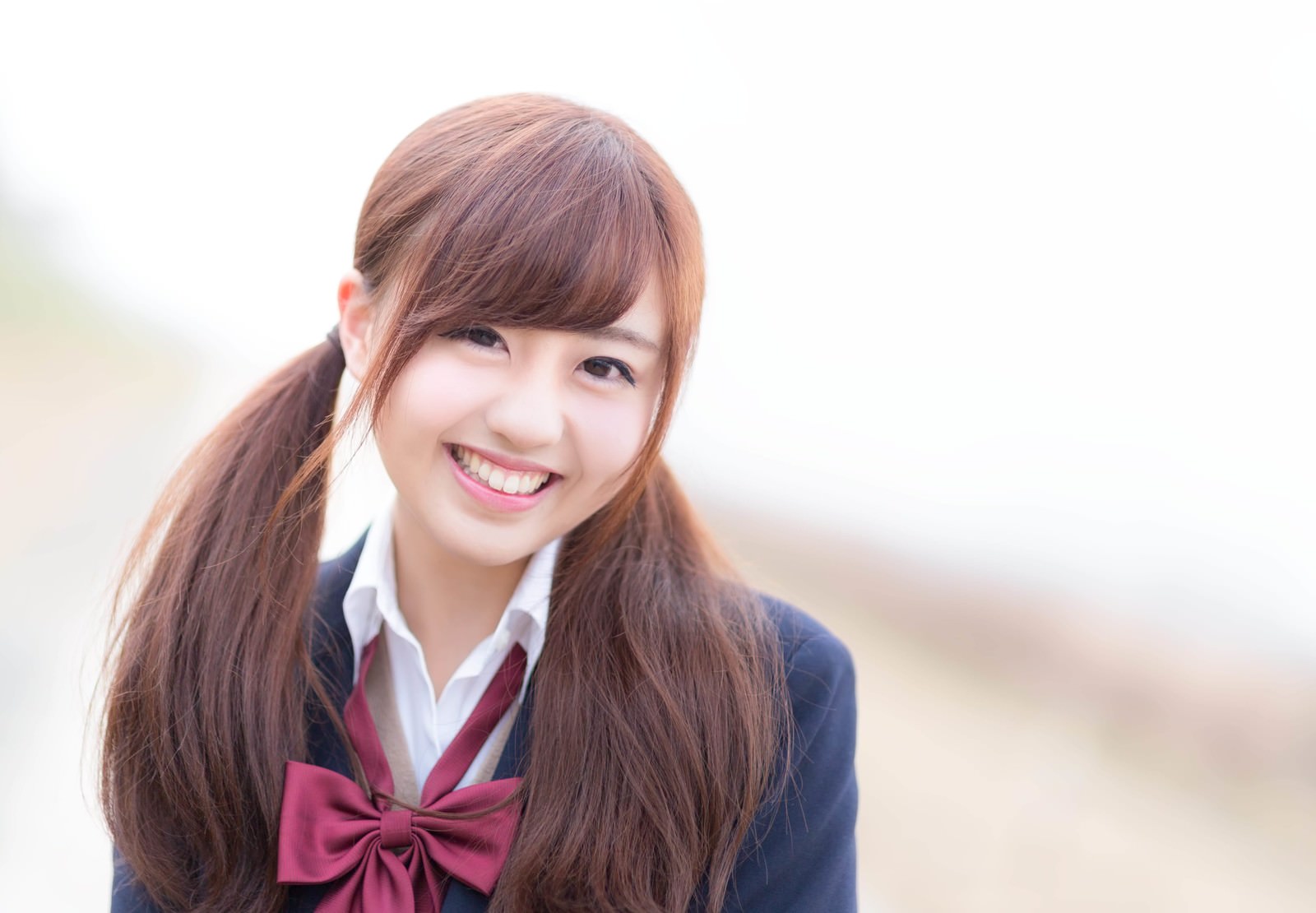 セーラー服姿の長髪女子高生が赤いリボンを身につけ、斜め上を向いて笑顔を見せている［モデル：河村友歌］