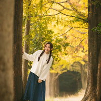 黄葉の並木道を歩く三つ編みの女性、秋の自然風景の写真