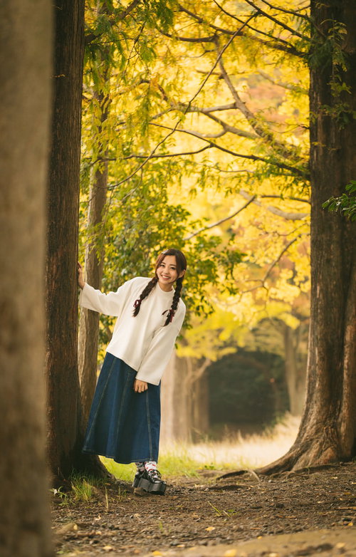 黄葉の並木道を歩く三つ編みの女性、秋の自然風景