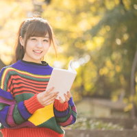 読書の秋、紅葉に包まれるマルチカラーセーターの女子の写真