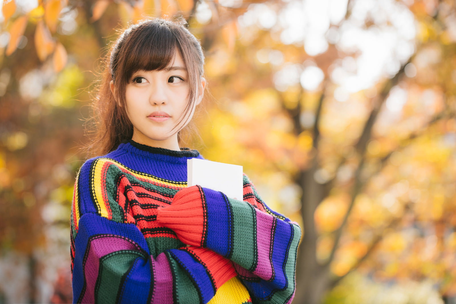 本を胸に抱きしめるニット姿の女性［モデル：河村友歌］
