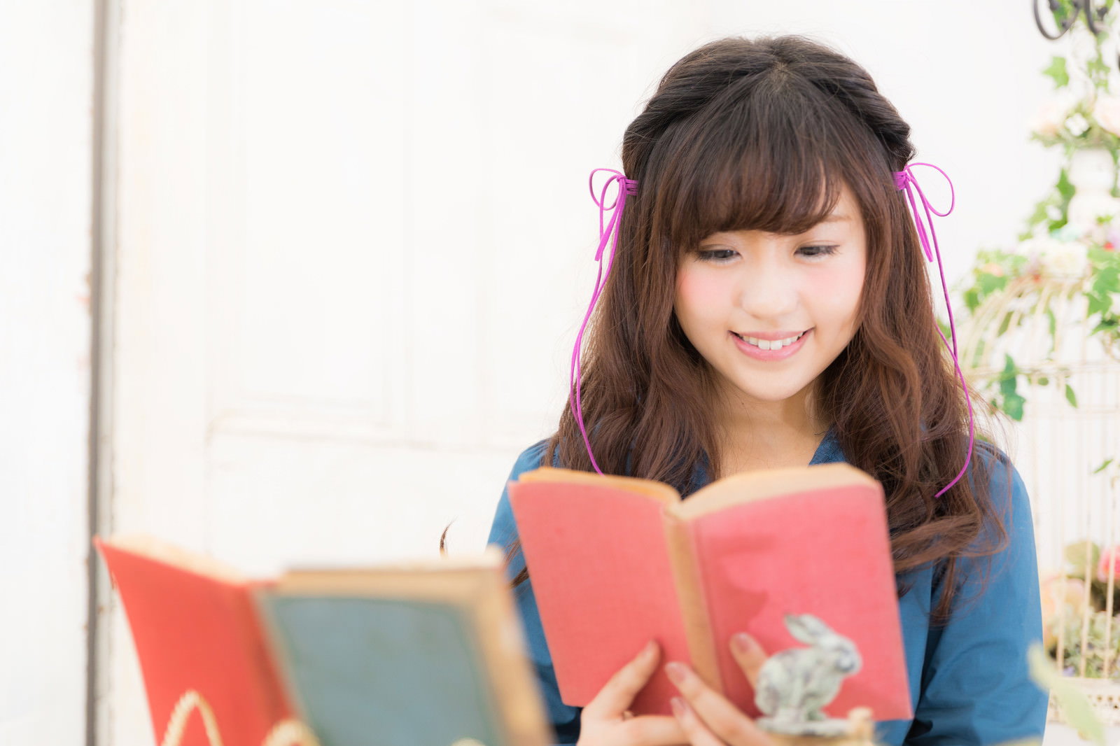 ピンクのリボンをつけた女性が室内で本を読む［モデル：河村友歌］