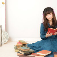 本と洋書に囲まれてふんわり読書する女性のリラックスシーンの写真