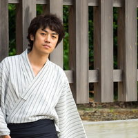 浴衣姿で夏祭りに来た男性が木製の柵の前に座るの写真