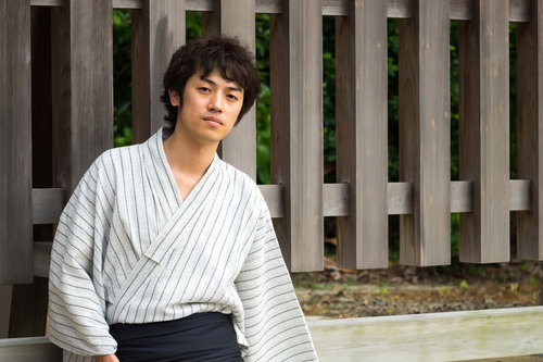 浴衣姿で夏祭りに来た男性が木製の柵の前に座る