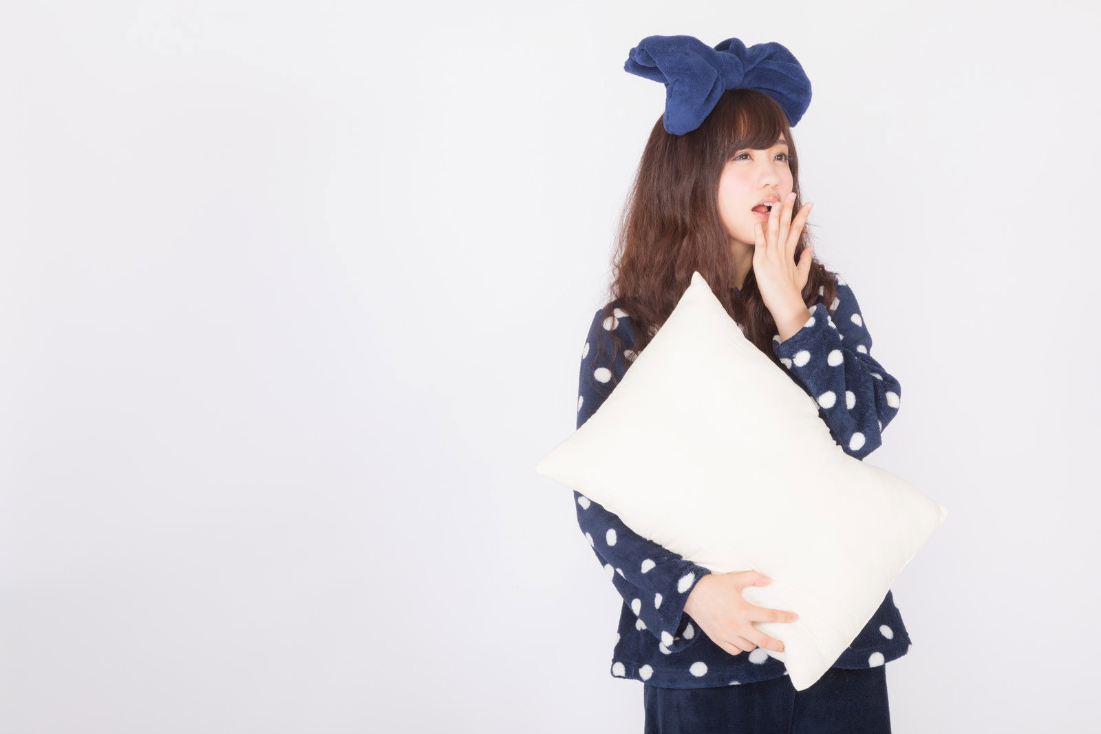 白い背景で枕を抱きながら大きくあくびするパジャマ姿の女性［モデル：河村友歌］