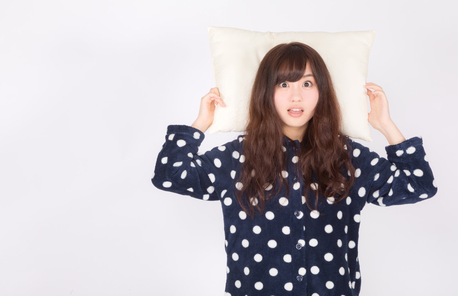 ドット柄のパジャマを着て枕を持ち驚いた表情の女性［モデル：河村友歌］
