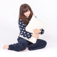 白い枕を抱いて眠そうな表情のパジャマ姿の女性の写真