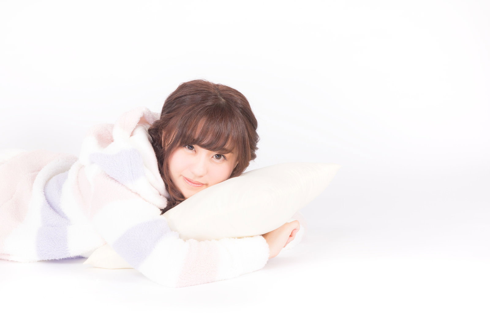 白い背景でクッションを抱きしめながら横になるパジャマ姿の女性［モデル：河村友歌］