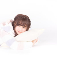 クッションを抱きしめながら横になるパジャマ姿の女性の写真