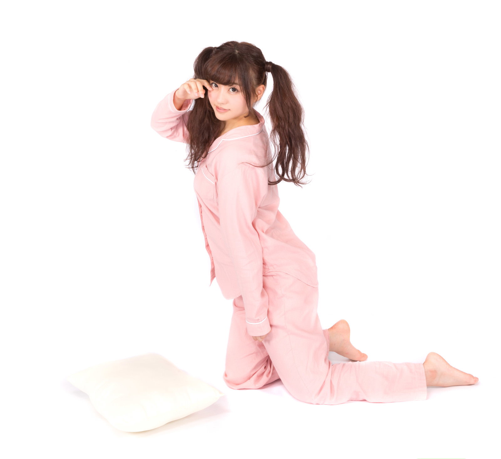 ピンク色のパジャマを着たツインテールの女性が白い枕を抱えて眠そうにしている［モデル：河村友歌］