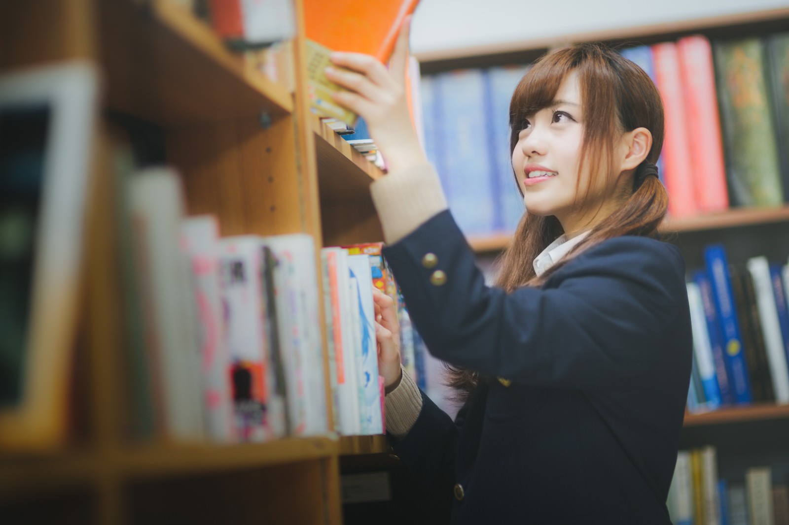 図書室の本棚から本を選ぶ学ラン姿の女性［モデル：河村友歌］