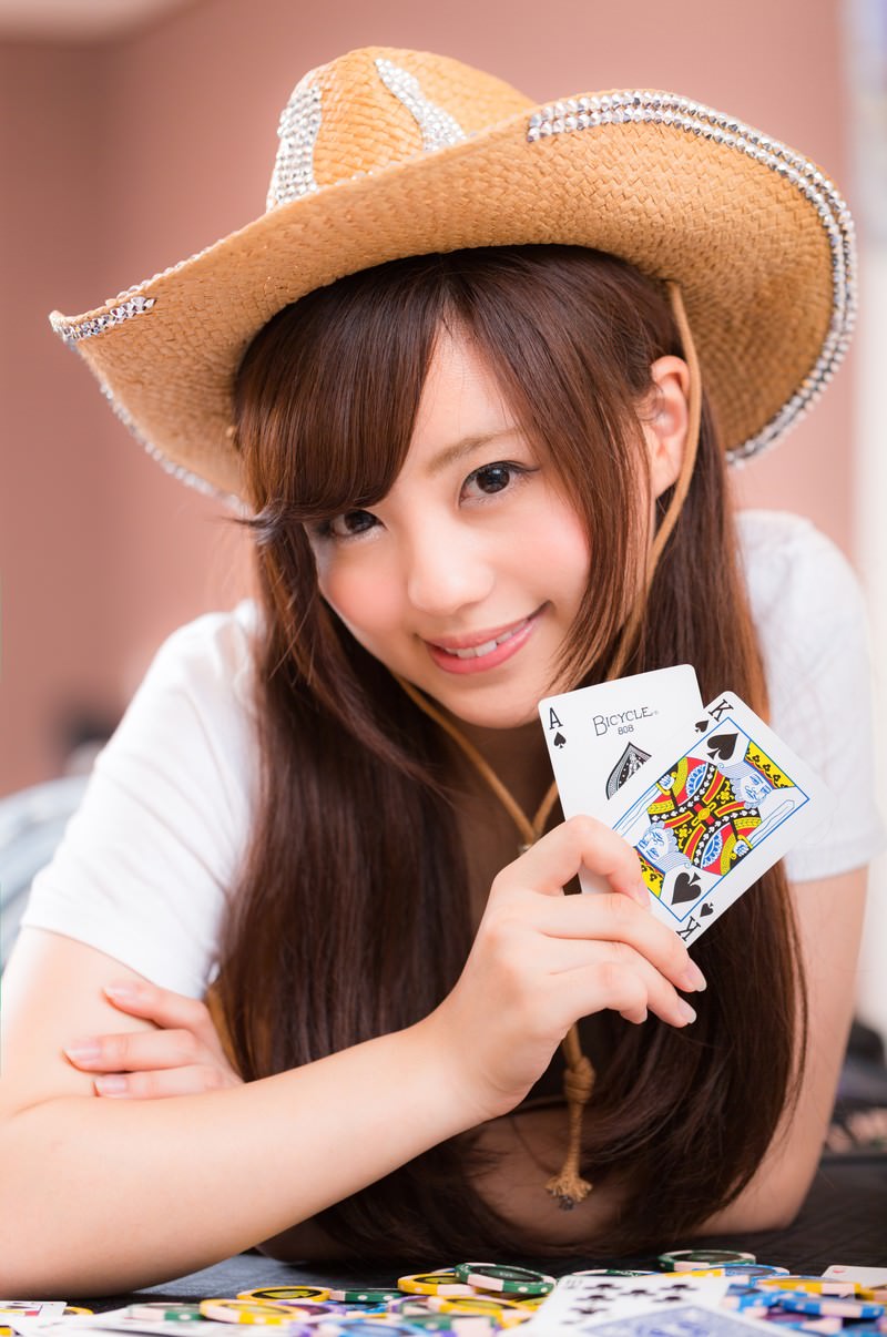 麦わら帽子をかぶったカウガール姿の女性がトランプを持ち、カジノテーブルでカードを見せている［モデル：河村友歌］