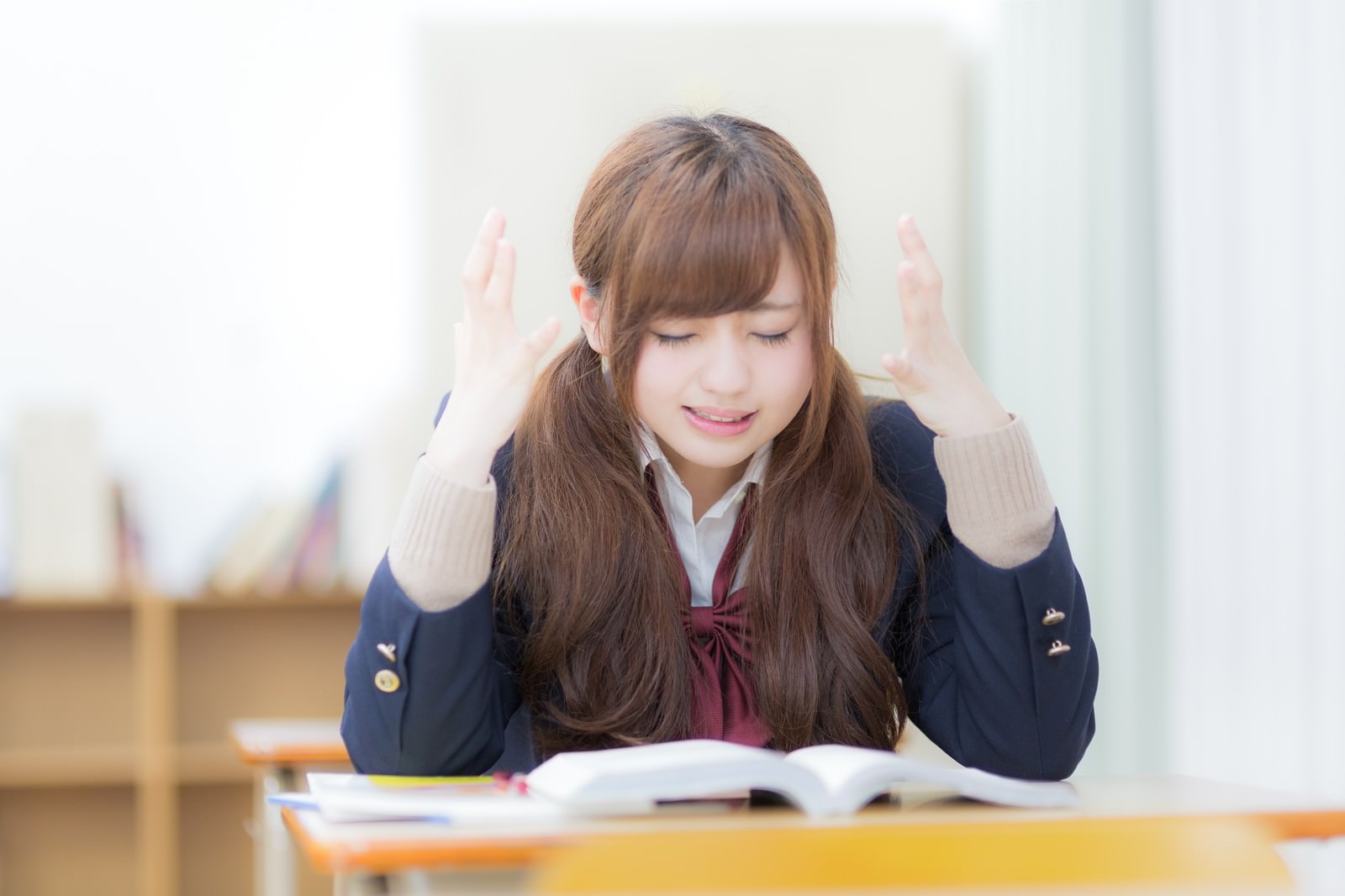 テーブルで両手を上げて困惑する女子高生［モデル：河村友歌］