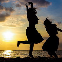 焼けたオレンジ色の空と浜辺で歓喜する二人のシルエットの写真