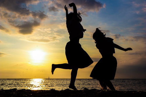 焼けたオレンジ色の空と浜辺で歓喜する二人のシルエット