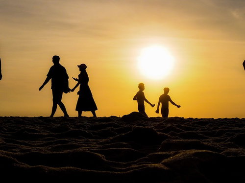 夕暮れの浜辺を行き交う人々のシルエット、夕日と砂浜